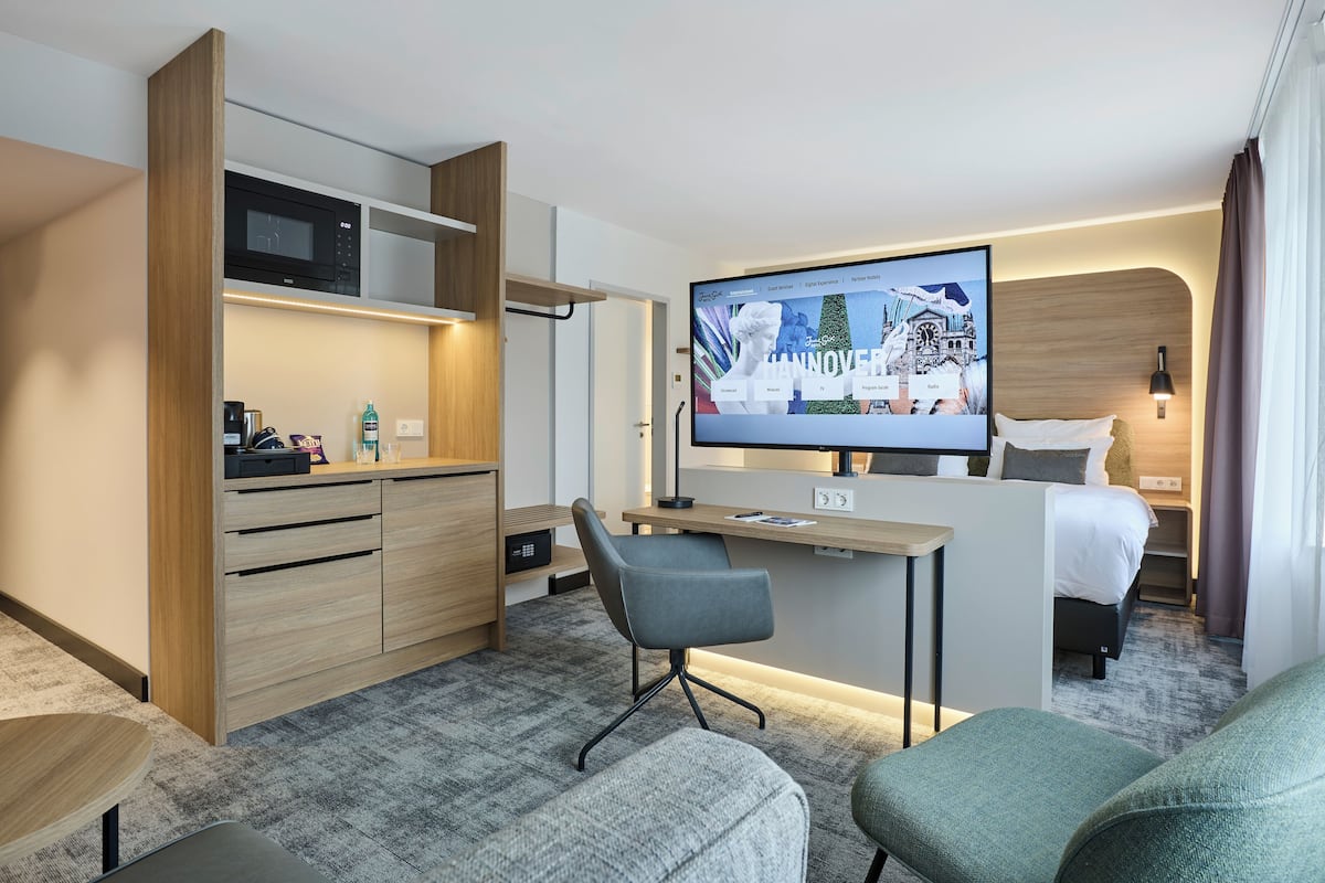 Ein modernes Hotelzimmer mit Küchenzeile, einem Flachbildfernseher, einem Bett und einer Sitzecke.