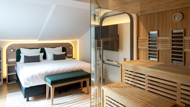Een moderne hotelkamer met een groot bed, een bankje, een sauna en een houten wandpaneel.