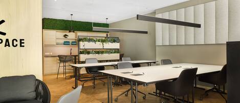 A modern meeting room with a large table, chairs, a sofa, and a kitchenette area.