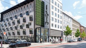 Een modern hotel met een glazen gevel, balkons met planten en een rood fietspad.