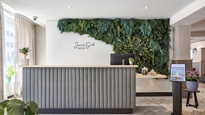 Een receptiebalie met een verticale tuin als achtergrond, een digitaal scherm en een potplant.