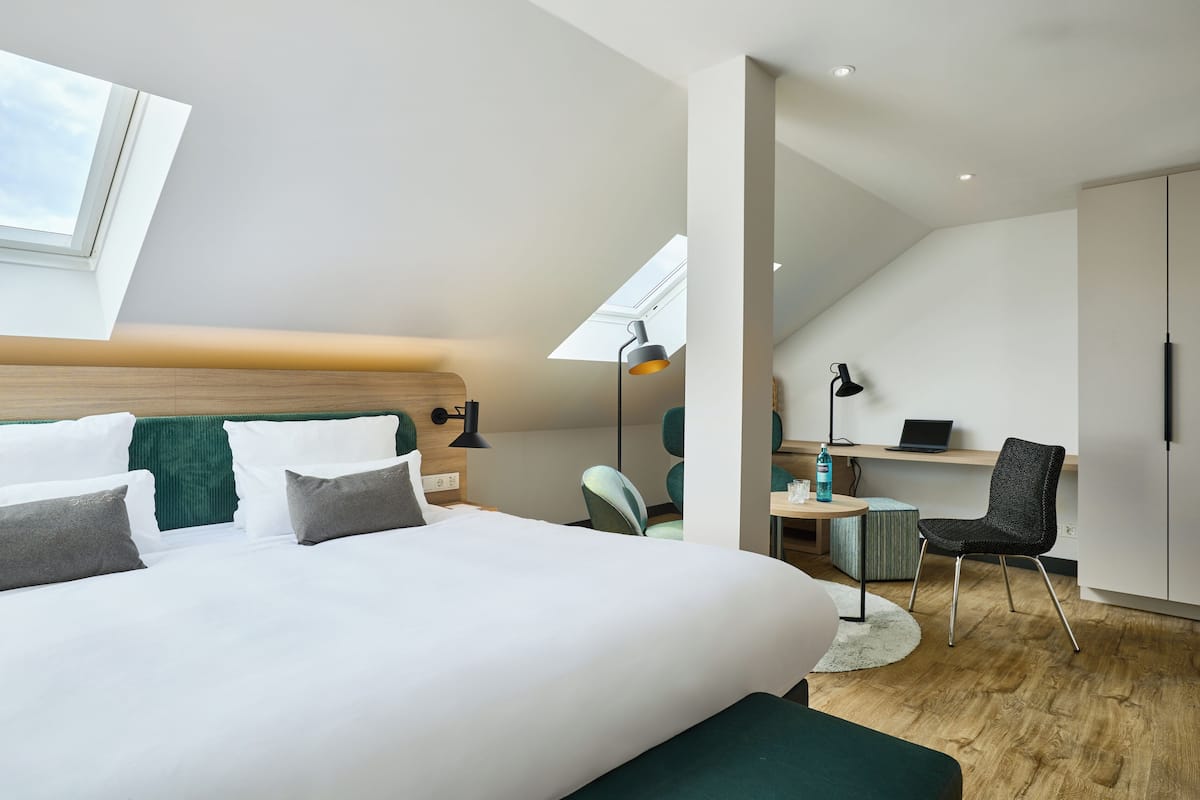 Ein modernes Hotelzimmer mit einem großen Bett, einem Schreibtisch, einem Stuhl und einem Oberlicht.