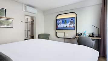 Habitación de hotel con una cama grande, un escritorio con computadora, una silla y un televisor montado en la pared que muestra una imagen panorámica.
