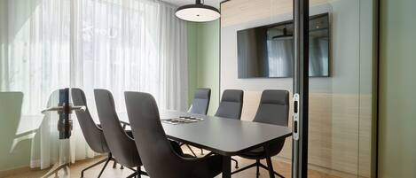 A conference room with a long table, six chairs, and a large window with sheer curtains.