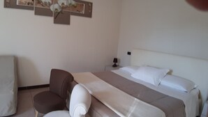 Una habitación de hotel con cama, una silla, una mesita de noche y un cuadro colgado en la pared.