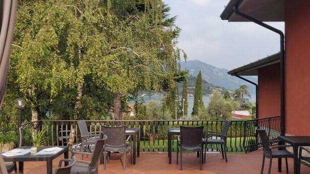 Un patio al aire libre con mesas y sillas, vista a un lago y una montaña al fondo.