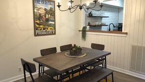 A dining area with a wooden table, chairs, and a chandelier. A poster of 'The Old Mill' is on the wall. - Modern 2BD Condo Near TOWN! Fire Pit + Pool Table (Pigeon Forge)