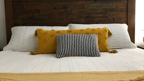 A bed with a wooden headboard, white bedding, and two pillows, one yellow and one striped. - Modern 2BD Condo Near TOWN! Fire Pit + Pool Table (Pigeon Forge)