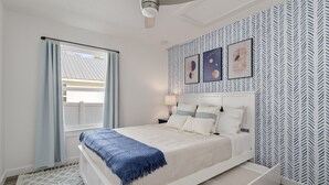 Ein Schlafzimmer mit einem Bett, einem Deckenventilator, einem Fenster mit Vorhängen und einer Wand mit Muster.