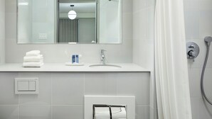 Un baño moderno con inodoro, lavabo, espejo, ducha y espacio para toallas.