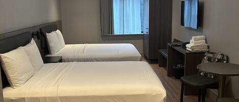 Ein Hotelzimmer mit zwei Betten, einem Schreibtisch, einem Stuhl, einem Fernseher und einem Fenster mit Vorhängen.