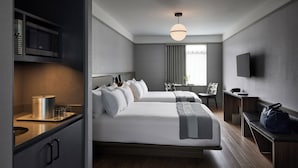 Habitación de hotel moderna con una cama grande, mesitas de noche, un escritorio, una silla, un televisor y una ventana con cortinas.