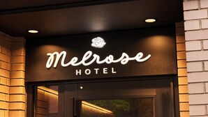 El exterior del Melrose Hotel con un llamativo letrero iluminado sobre la entrada.