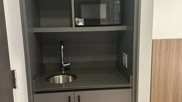 A compact kitchenette with a microwave, sink, and cabinets.