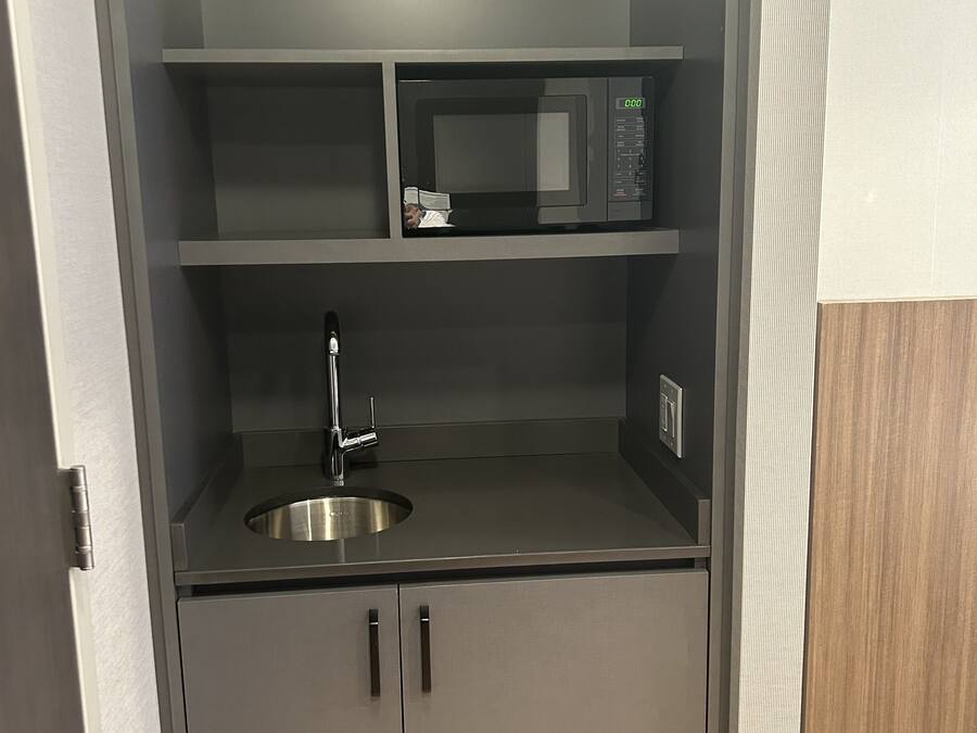 A compact kitchenette with a microwave, sink, and cabinets.