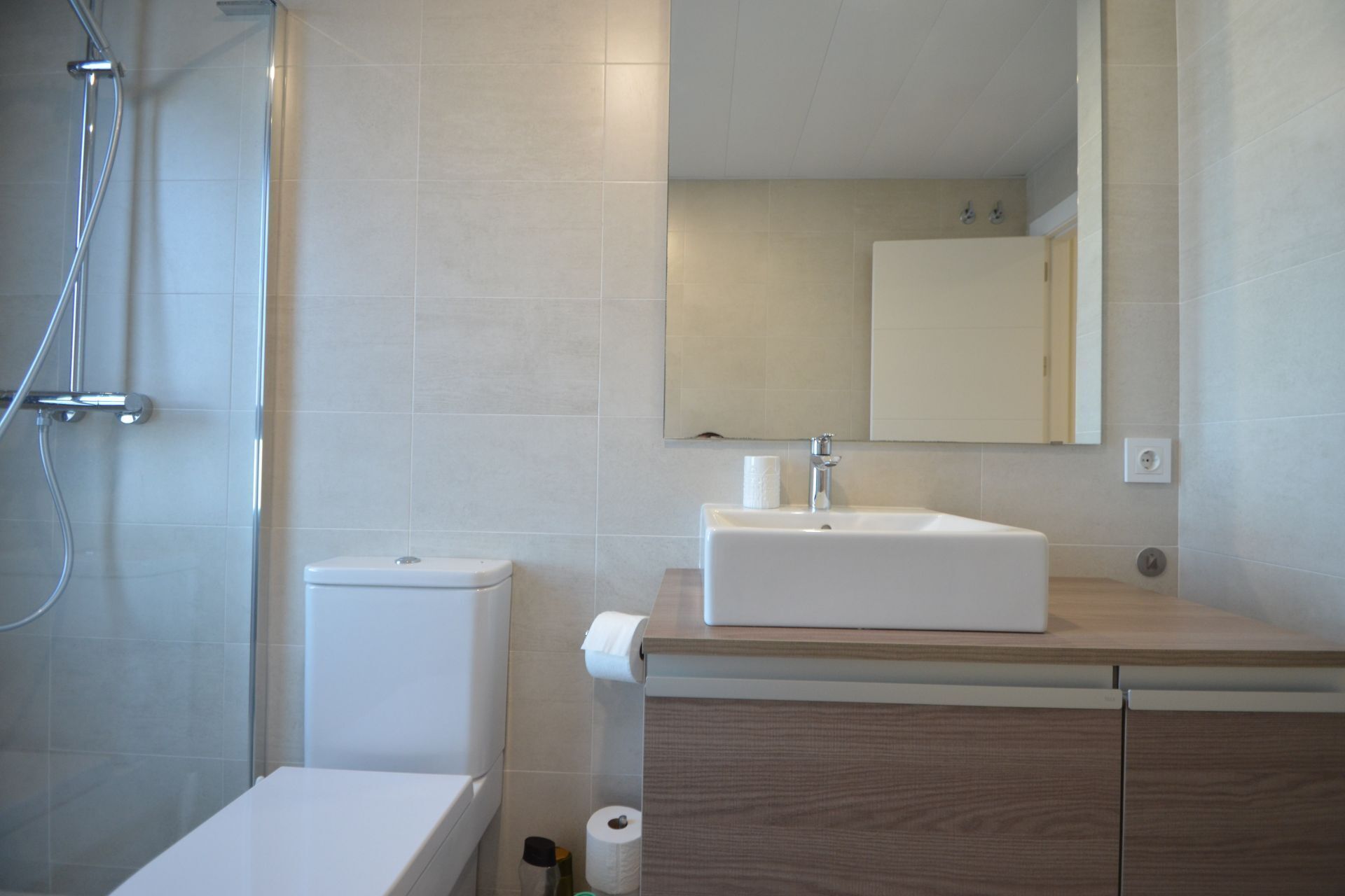 A modern bathroom with a shower, toilet, sink, and mirror.
