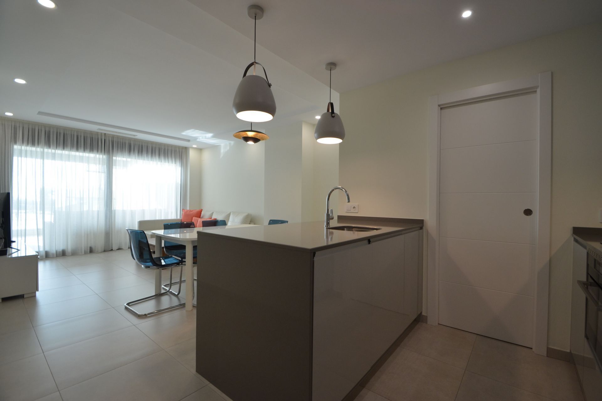 A modern kitchen with a central island, a dining area with a table and chairs, and a large window with curtains.