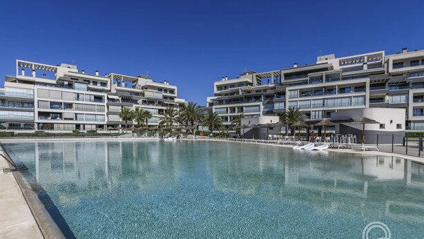 Un hôtel moderne doté d’une grande piscine, de nombreux balcons et de palmiers.