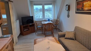 Ein gemütliches Wohnzimmer mit Fernseher, Esstisch und Stühlen.
