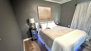 Ein Schlafzimmer mit Bett, Nachttisch, Lampe und einem an der Wand befestigten Kunstwerk.