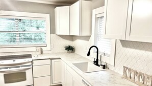 Eine moderne Küche mit weißen Schränken, einem Einbauofen, einem Spülbecken mit schwarzem Wasserhahn und einem Fenster mit Jalousien.