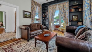 Ein Wohnzimmer mit braunem Ledersofa, einem Holztisch und einem Bücherregal voller Bücher und Dekoration.