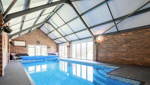 An indoor swimming pool with a clear blue tiled floor, a brick wall, and a metal roof structure. - Home Farm (Saint Asaph)
