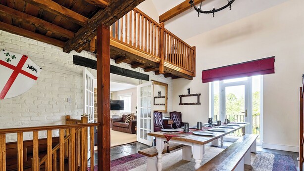 A dining area with a long wooden table set for a meal, a staircase with wooden railings, and a flag on the wall. - Home Farm (Saint Asaph)