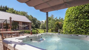 A hot tub with a wooden deck, a brick building, and a hedge in the background. - Home Farm (Saint Asaph)