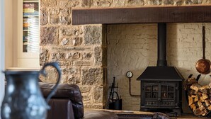 A cozy living room with a stone wall, a fireplace, a leather sofa, and a table with a metal pitcher. - Home Farm (Saint Asaph)