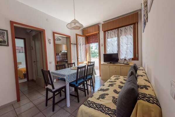 A compact living space with a dining area, a sofa, a television, and a kitchen area. - Charming Apartment Near the spa - Beahost (San Michele al Tagliamento)