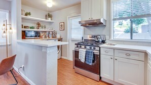 A kitchen with white cabinets, a stove, a microwave, and a window with blinds.
