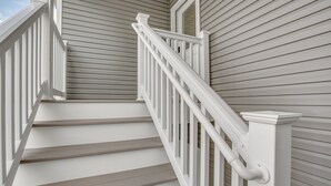 Un escalier avec des rampes blanches et des marches en bois, menant à une porte surmontée d’une fenêtre.