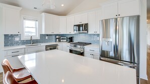 Une cuisine moderne avec des meubles blancs, des appareils en acier inoxydable et un grand îlot central.