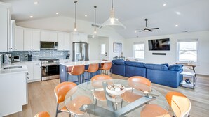 Une cuisine moderne avec des meubles blancs, des appareils en acier inoxydable et un coin repas agrémenté de chaises orange et d’une table en verre.