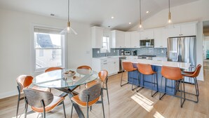 Une cuisine moderne avec des meubles blancs, un îlot central doté de tabourets et des luminaires suspendus.