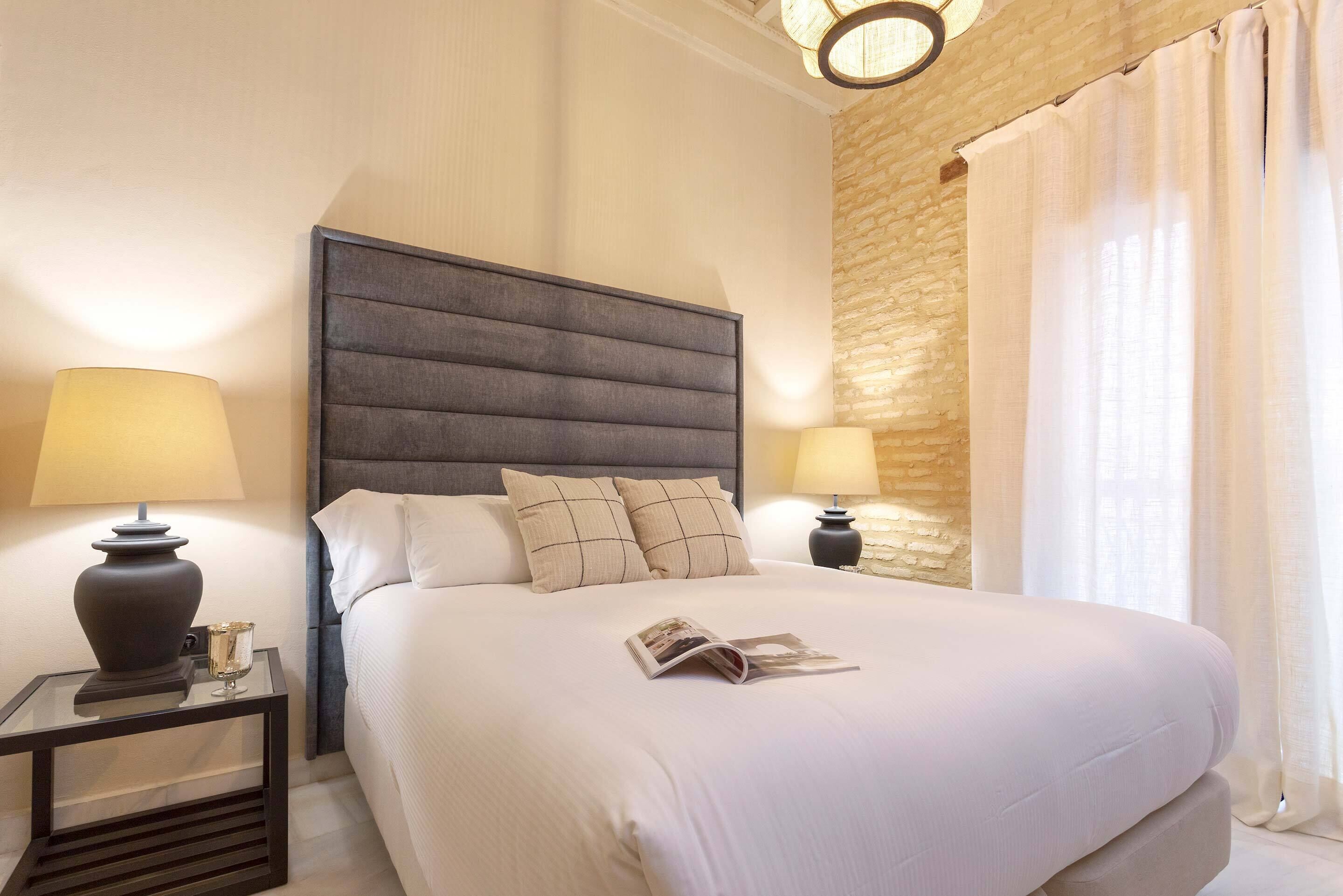 A neatly made bed with a headboard, two bedside tables with lamps, and a stone wall.