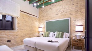 Un dormitori amb un llit gran, dues taules de nit, un calaix i una finestra amb cortines, i una paret de maó.