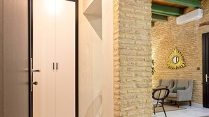 Habitació amb sostre de fusta, paret de maó, porta blanca i una petita zona d'estar amb una cadira i un sofà.