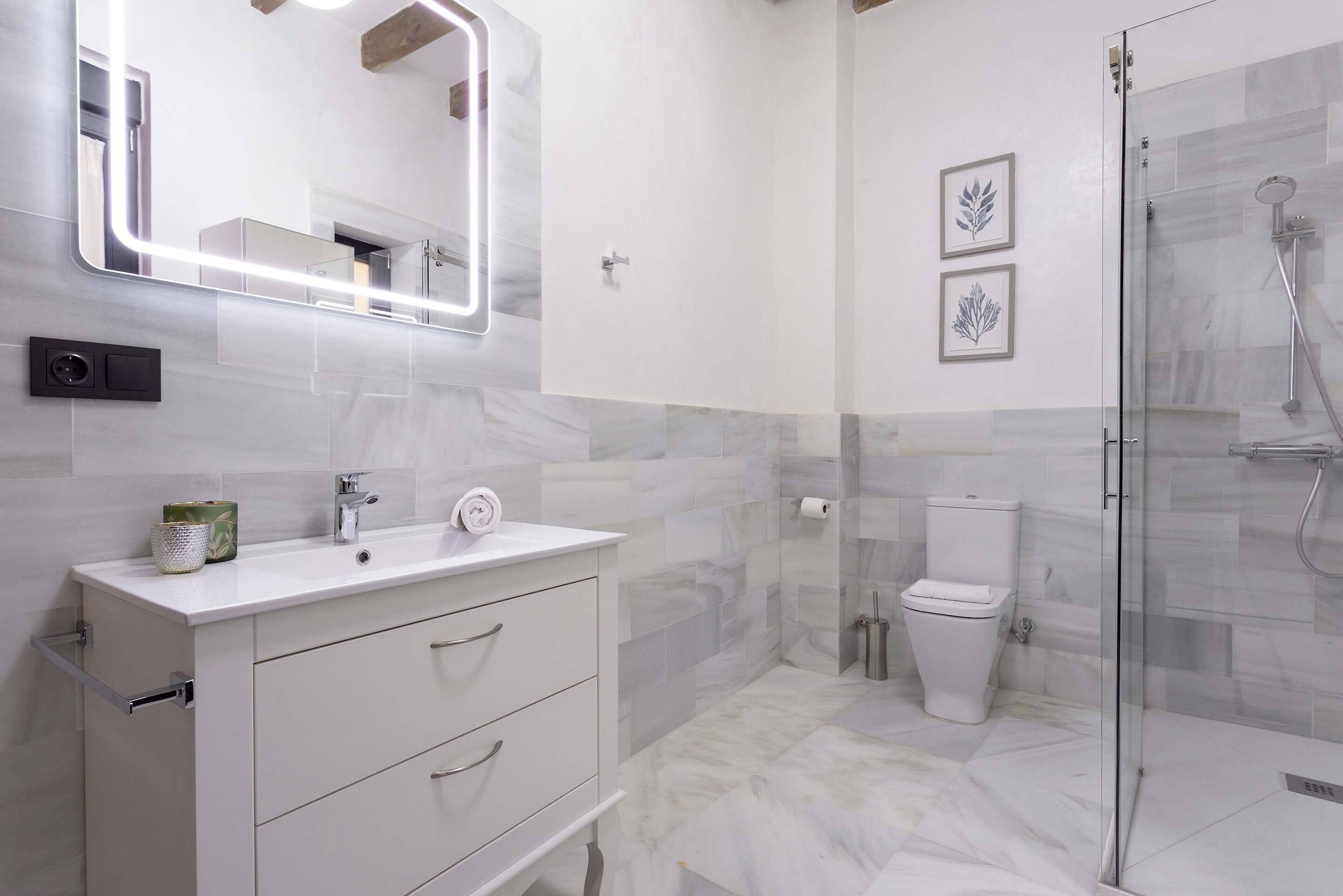 A modern bathroom with a white vanity, a glass shower enclosure, and marble flooring.