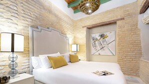 A hotel room with a large bed, two bedside lamps, a modern chandelier, and a brick wall. - Genteel Home Acetres III (Seville)
