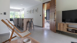 Een moderne woonkamer met een houten tv-meubel, een grote flatscreen televisie en een eethoek met een tafel en stoelen.