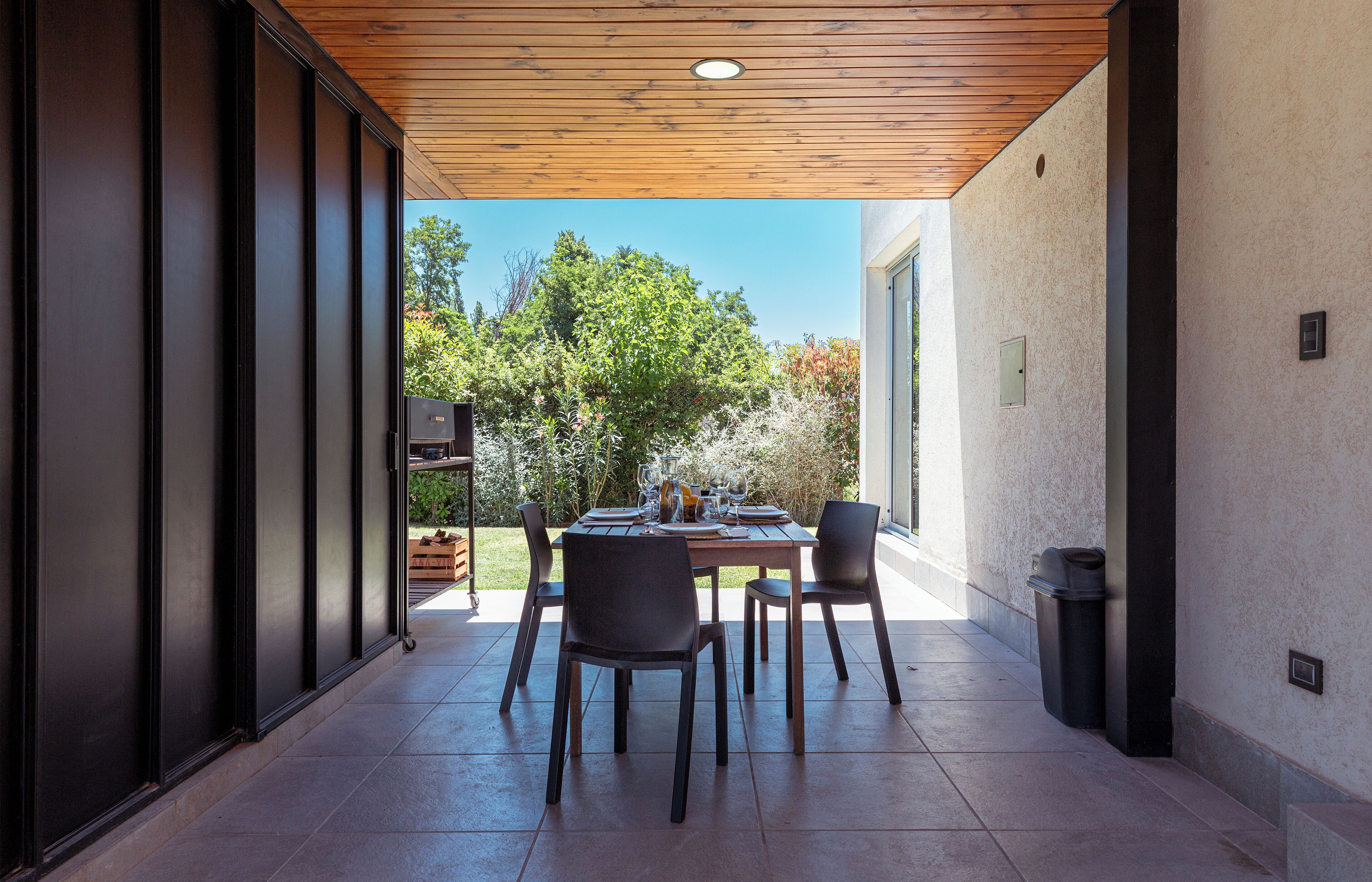 Une terrasse extérieure avec un plafond en bois, une table dressée pour quatre personnes et des chaises.