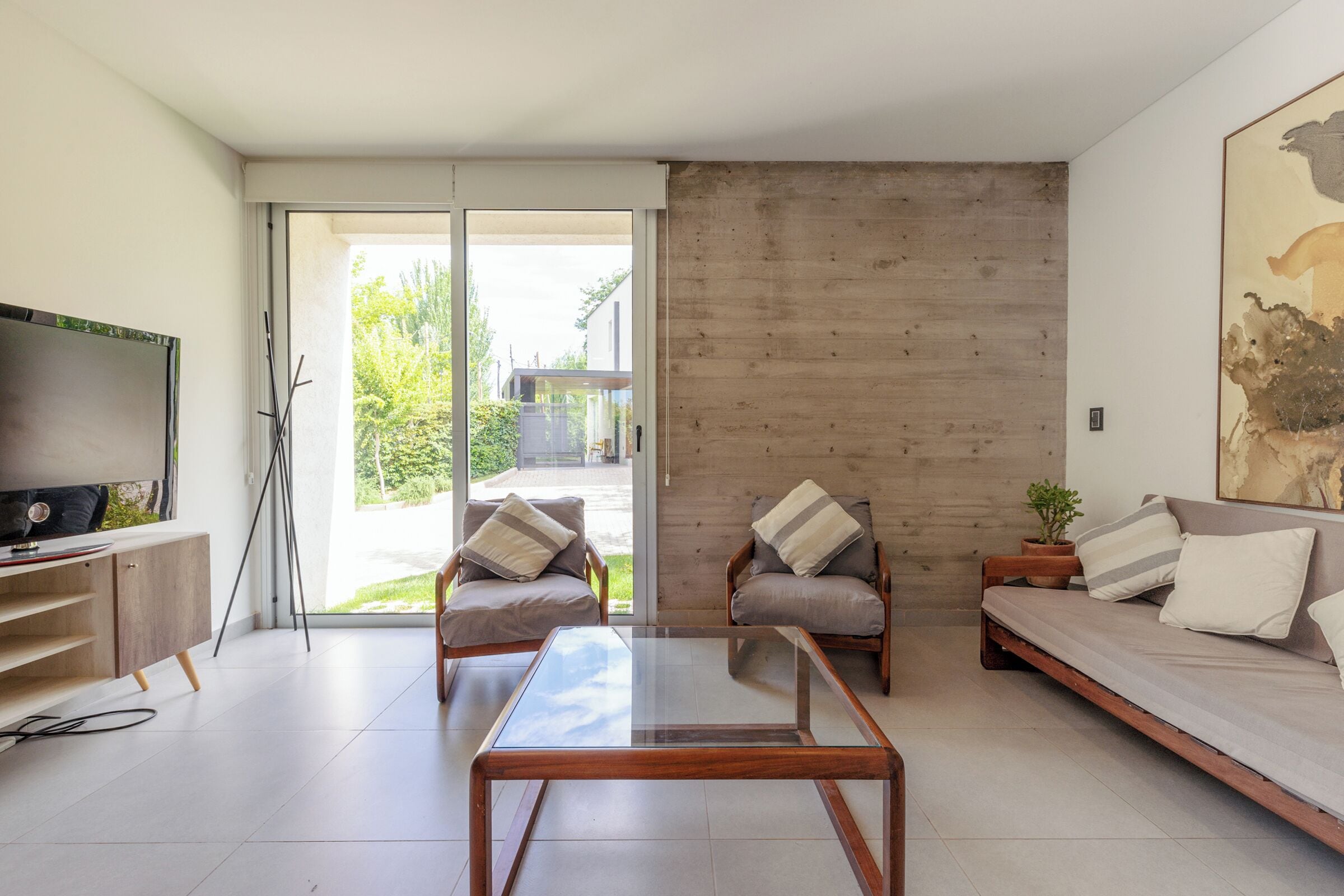 A modern living room with a glass coffee table, two armchairs, a sofa, a flat-screen TV, and a wooden accent wall.