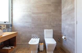 Un baño con bidé, inodoro y tocador de madera con lavamanos.
