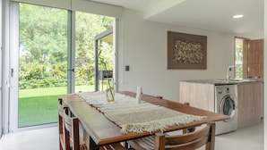 Een moderne keuken met een ingebouwde wasmachine, een eethoek met een houten tafel en banken, en een schuifpui naar een tuin.