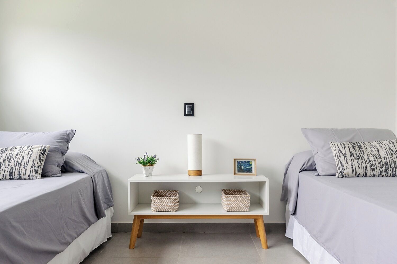 Een slaapkamer met twee bedden, een nachtkastje, een lamp, een kleine plant en twee fotokaders.