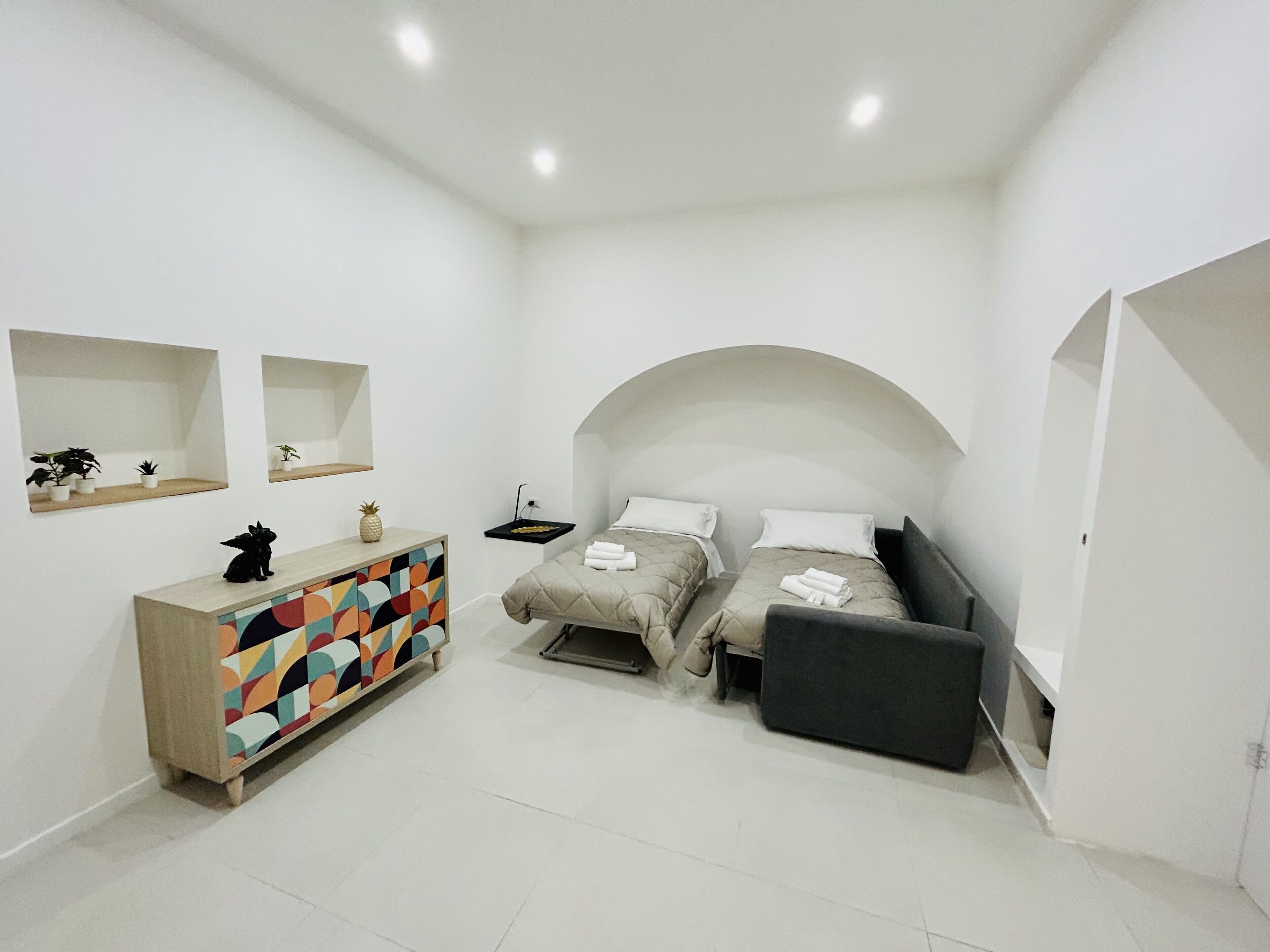 Une chambre moderne avec deux lits, une commode aux couleurs vives et une petite table décorée d’un ananas.