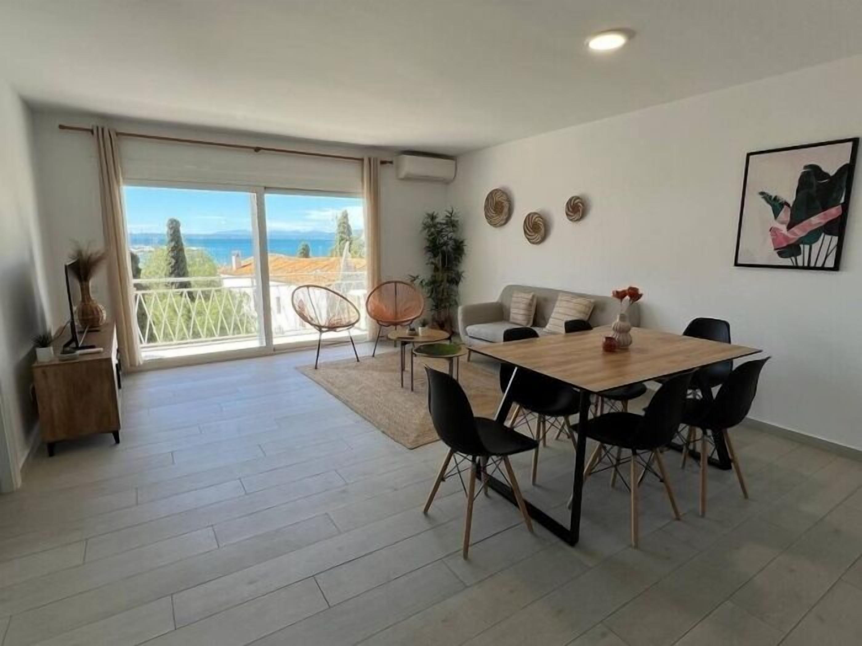 Een moderne woonkamer met een eethoek, grote schuifdeuren naar een balkon en uitzicht op zee.