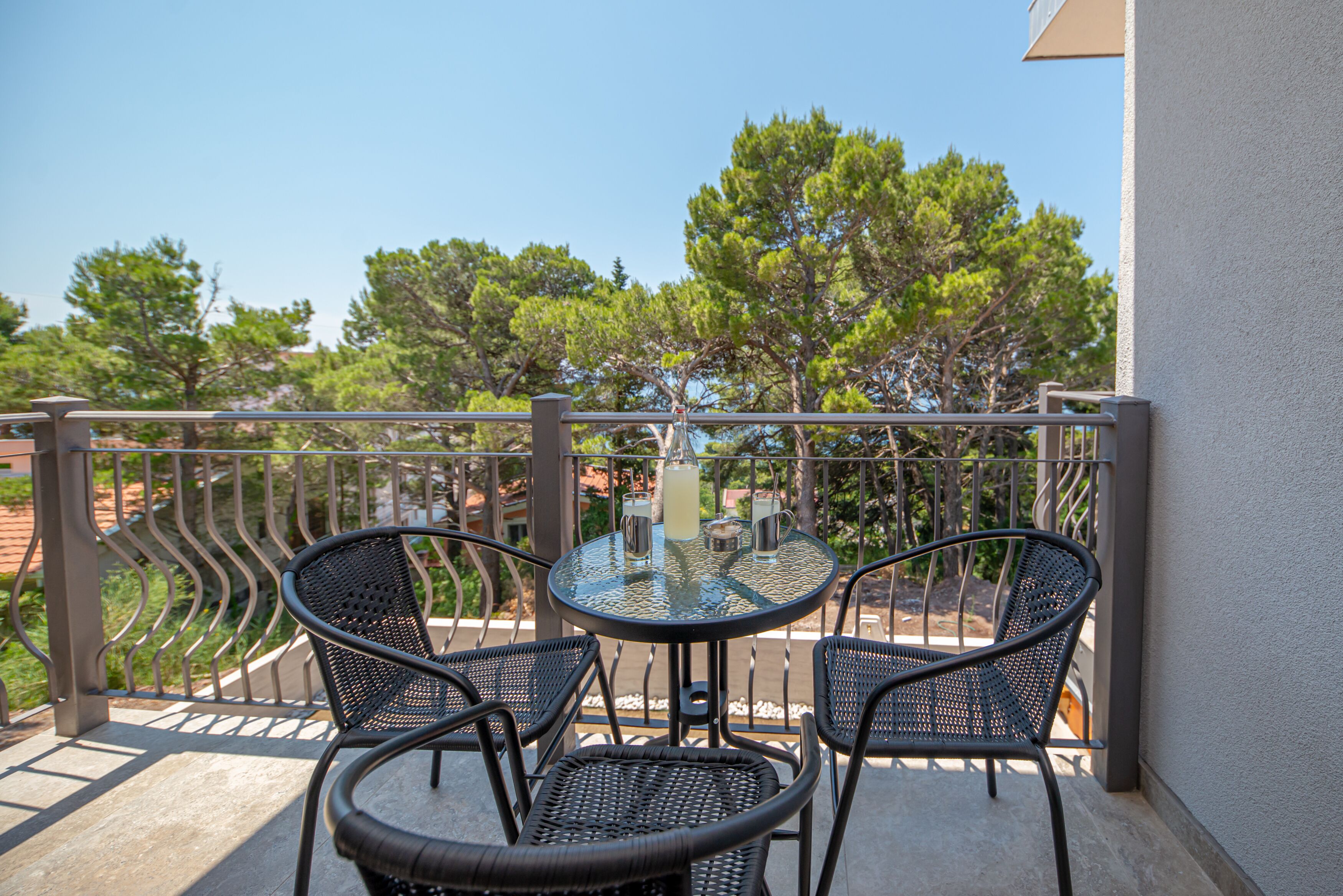 A balcony with a round table and two chairs, overlooking a garden with trees.